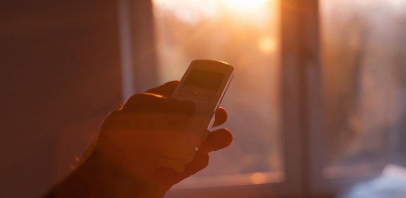 Mano con mando Konect apuntando a una ventana luminosa para controlar la persiana de forma remota